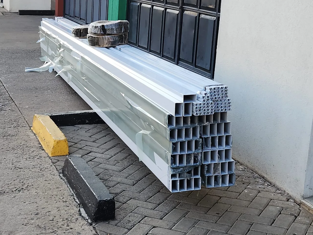 Imported aluminium box profiles and window sections stacked outside the EGZ workshop