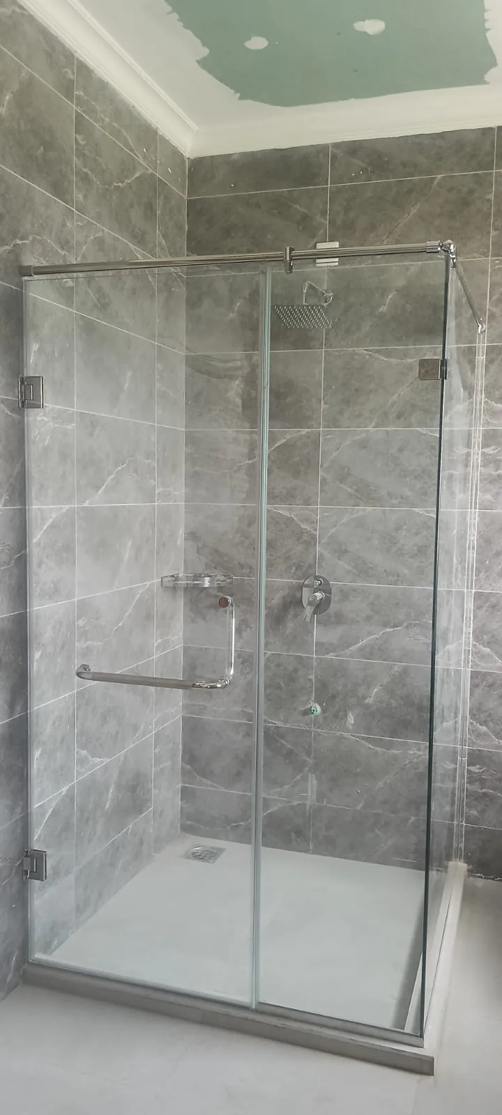 Semi-frameless hinged shower door fitted to a marble-tiled recess